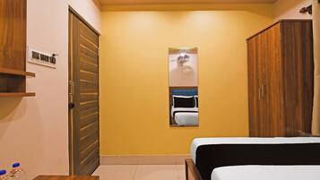 A bedroom with a bed, a wardrobe, a mirror, and a small table with water bottles.