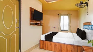 A hotel room with a bed, a TV mounted on the wall, a window with curtains, and a ceiling fan.