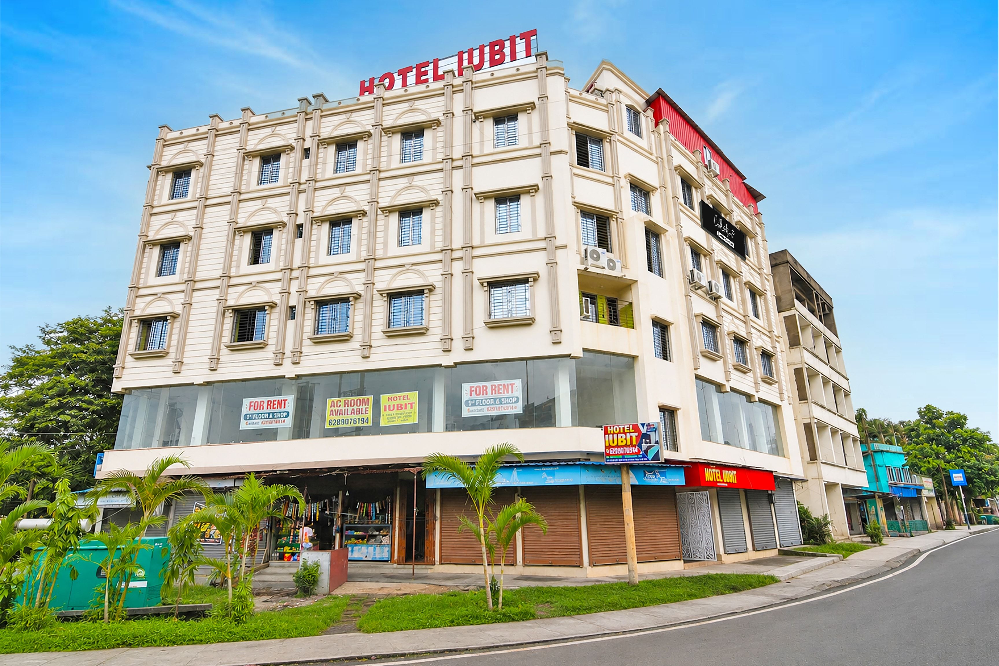 A multi-story hotel with a prominent 'HOTEL IUBIT' sign, multiple ground-floor shops, and a variety of signage indicating available rooms and shops.