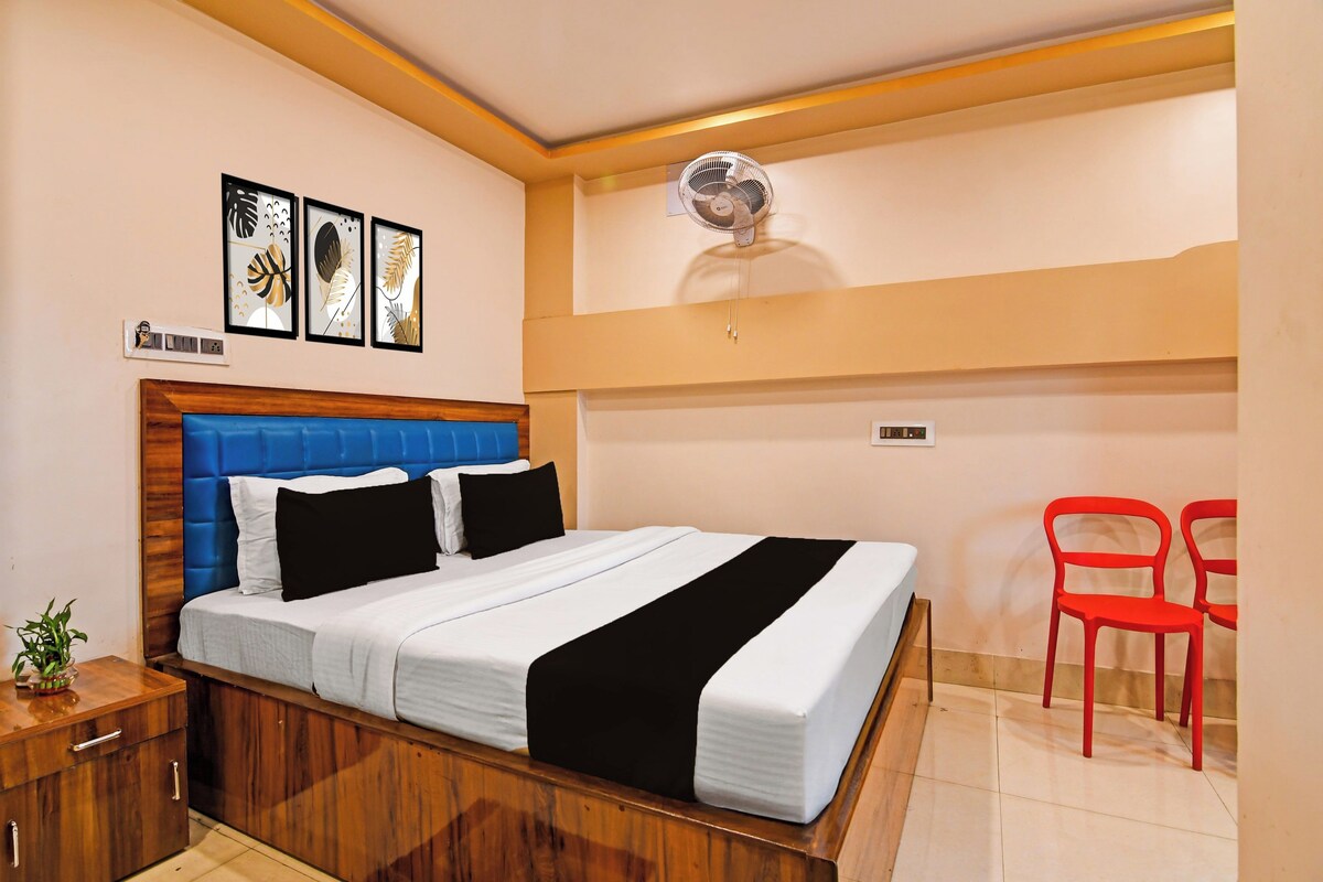 Una habitación de hotel con una cama, una mesita de noche, un enchufe en la pared, un ventilador de techo y un interruptor de luz en la pared.