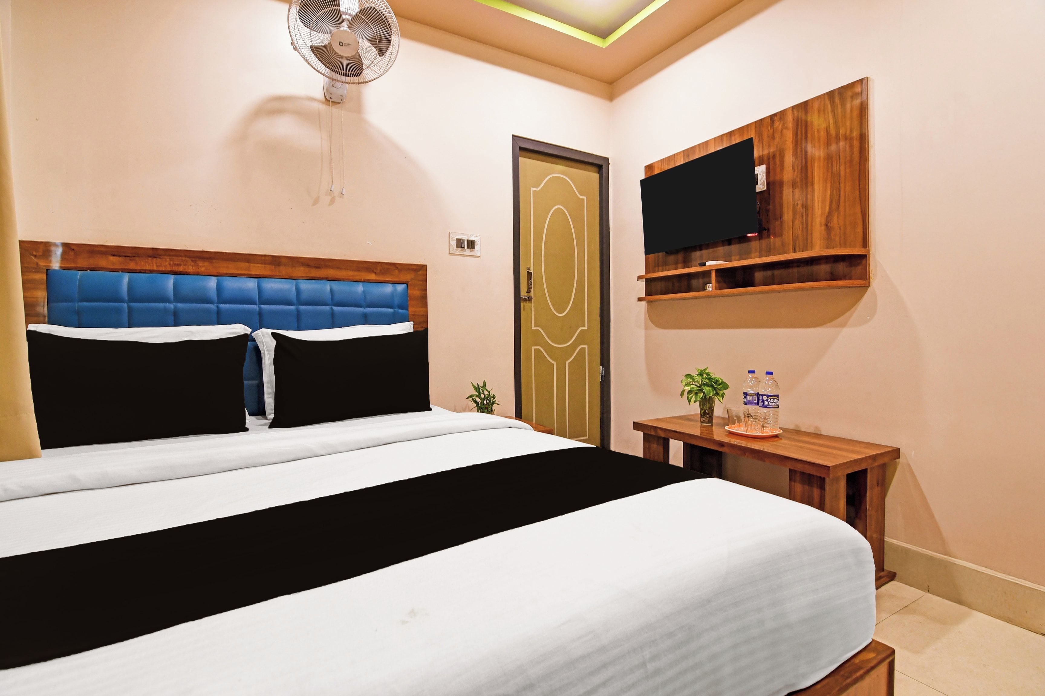 Une chambre à coucher avec un lit, une table de chevet, un téléviseur fixé au mur et une porte.