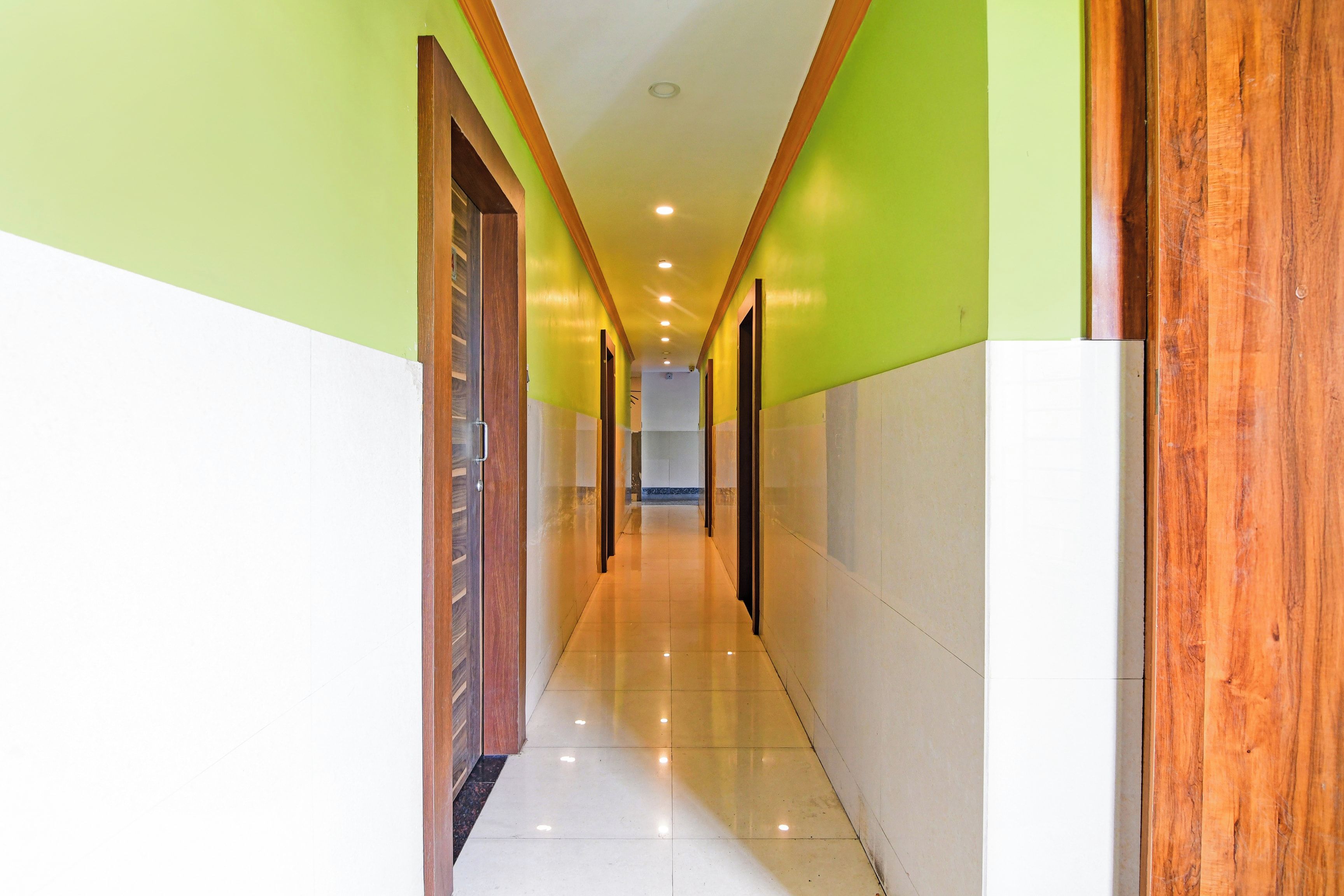 A corridor with a wooden door on the left, a tiled floor, and a green wall on the right.