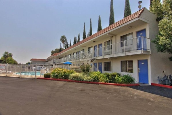 A motel with a swimming pool, a fenced parking area, and a red-tiled roof. - Stylish Full Beds|Pool|Free Wifi&TV (WEST SACRAMENTO)