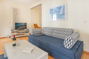 A living room with a blue sofa, a flat-screen TV, a wine bottle, and a book on a coffee table. - Delbrück Villas - House 2 D211 - on the Heringsdorf Promenade (Heringsdorf (Seebad))