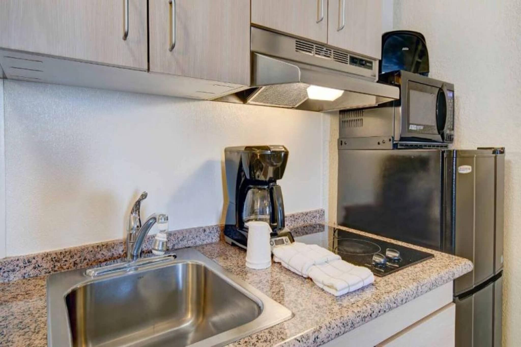 A kitchenette with a stainless steel sink, a coffee maker, a microwave, and a refrigerator.