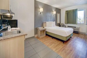 Una habitación de hotel con cama, un escritorio pequeño, un lavamanos y un ventanal con cortinas.
