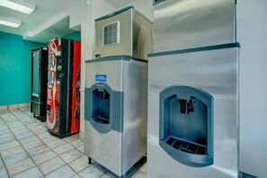 Une rangée de distributeurs d’eau en acier inoxydable dans un couloir, avec un sol carrelé et des murs de couleur turquoise.