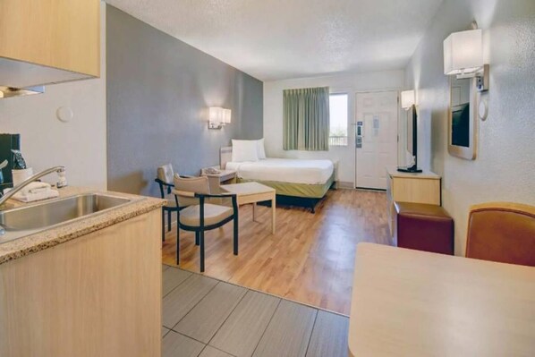 Une chambre d’hôtel de taille réduite, équipée d’une kitchenette, d’un lit, d’un bureau et d’une chaise.