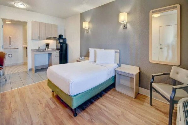 Una habitación de hotel con cama, mesitas de noche, una silla, un escritorio con computadora y un rincón americano.