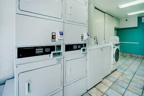 Une laverie équipée de plusieurs machines à laver et de plusieurs séchoirs, de terminaux de paiement et dotée d’un sol carrelé.