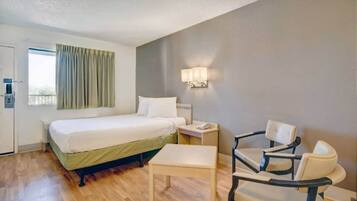 Quarto de hotel com cama, mesa de cabeceira, cadeira e janela com cortinas.