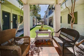 Un espacio al aire libre cubierto con mobiliario de mimbre, una mesa con un arreglo floral y vista a un edificio en el fondo.