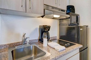 Una kitchenette equipada con un lavamanos de acero inoxidable, cafetera, microondas y refrigerador.