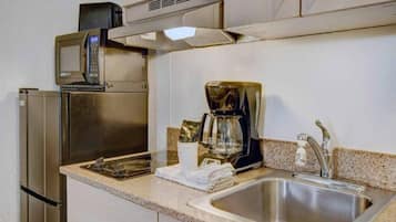 Eine Küchenzeile mit einem Edelstahlkühlschrank, einer Mikrowelle, einer Kaffeemaschine und einem Spülbecken.