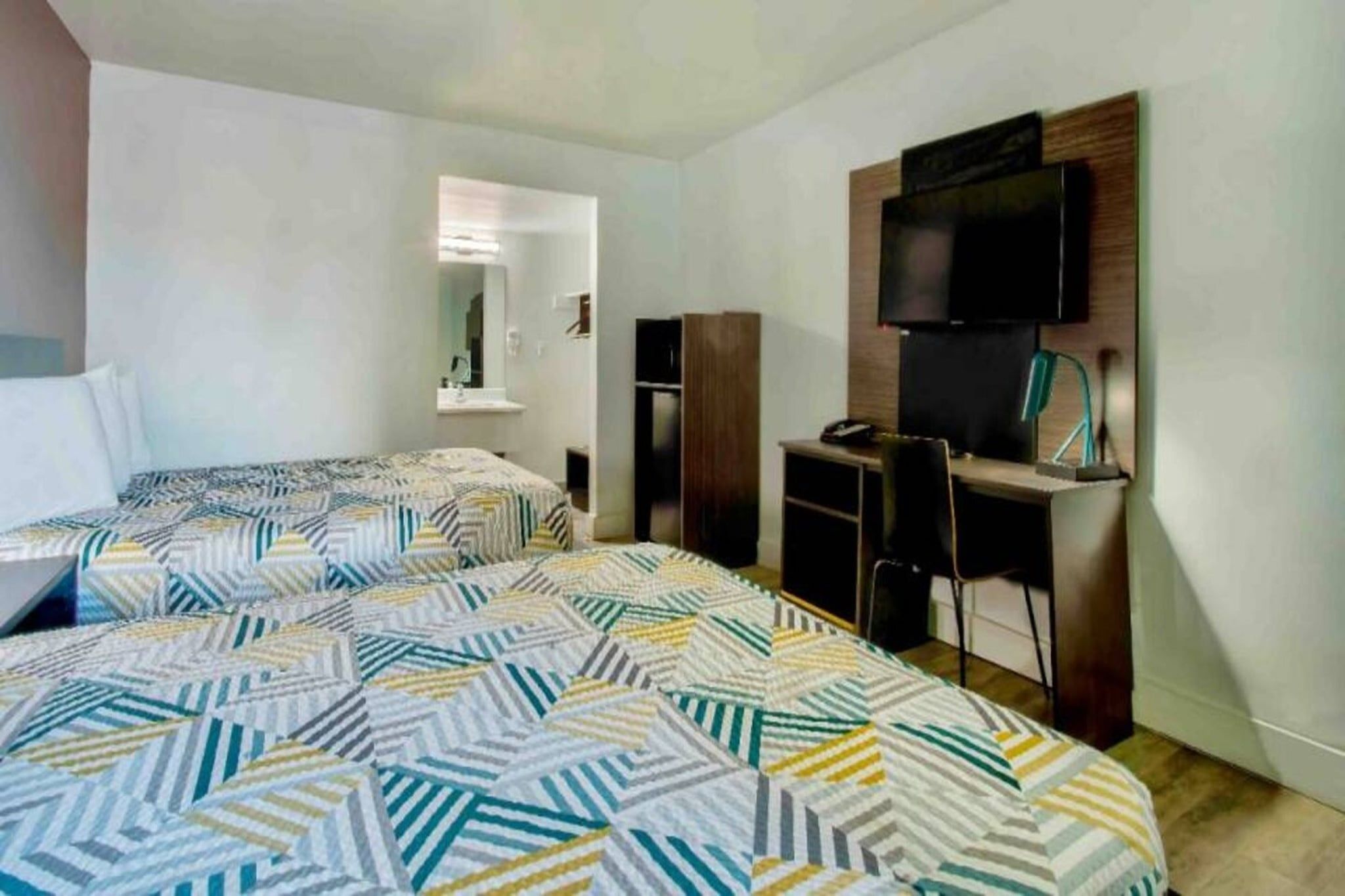 Une chambre d’hôtel avec deux lits, un bureau, une chaise, une télévision et un miroir.