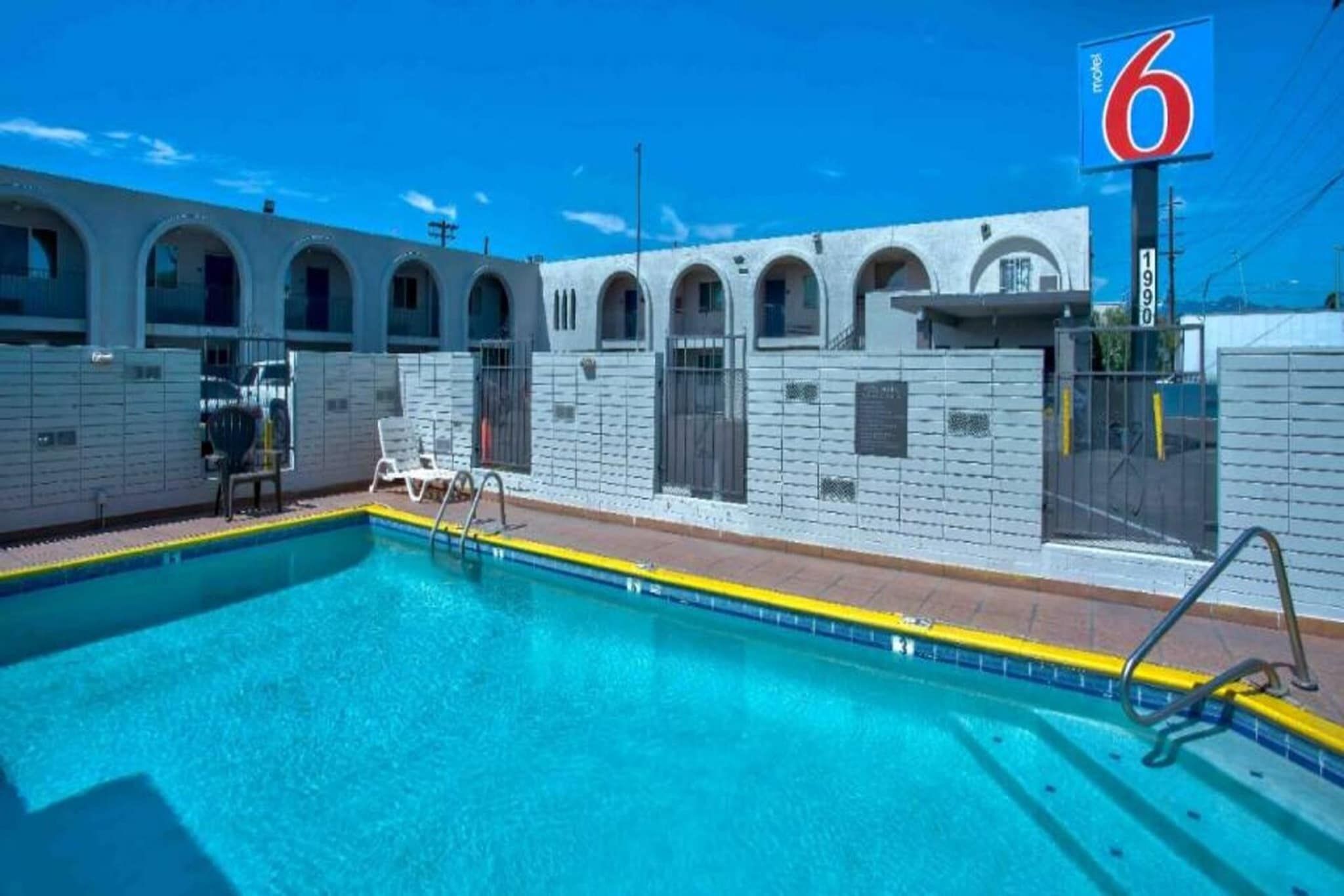 A swimming pool with a clear blue water, surrounded by a white building with arched windows and a sign indicating a motel.