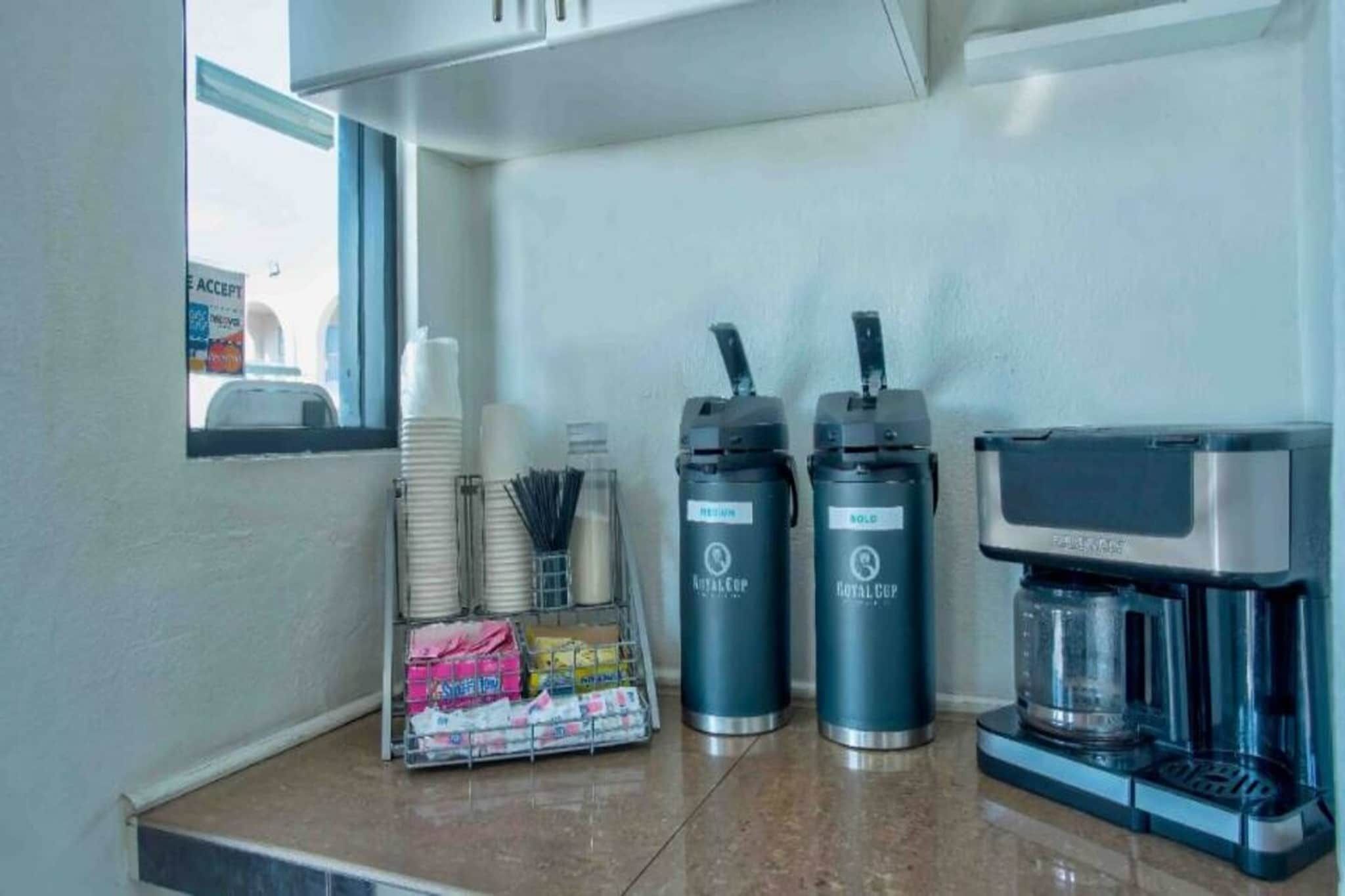 A coffee station with a coffee maker, two thermos cups, and a stack of disposable cups.