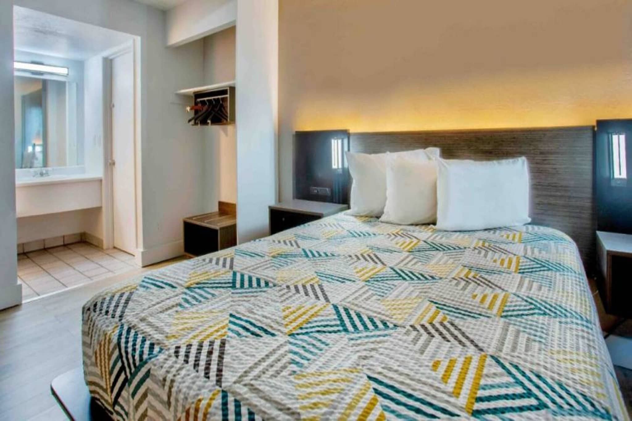 Habitación de hotel con una cama grande, una mesita de noche, un armario y un espejo.