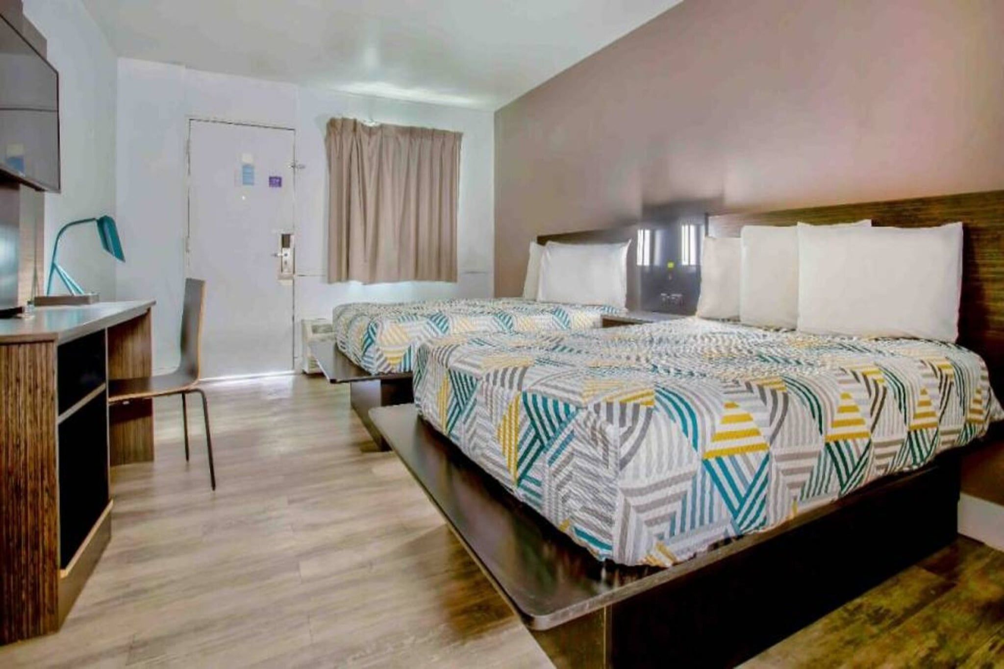 A hotel room with two beds, a desk, and a chair.