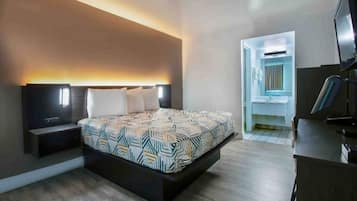 A modern bedroom with a large bed, bedside tables, a desk with a chair, and a TV.