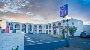 A motel with a row of arched windows, a parking lot, and a sign indicating the number 6.