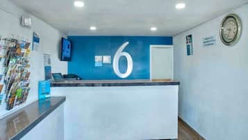 A reception desk with a large number '6' on the wall, a clock, and a magazine rack.