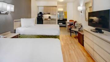 A hotel room with two beds, a television, a desk, and a kitchenette in the background.