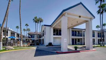 A hotel with a covered entrance, palm trees, and a parking lot.