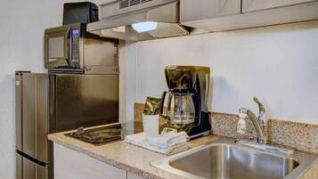 A kitchenette with a stainless steel refrigerator, microwave, coffee maker, and a sink.