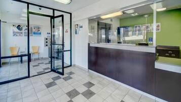 A reception area with a glass partition, a check-in counter, and a seating area with chairs.