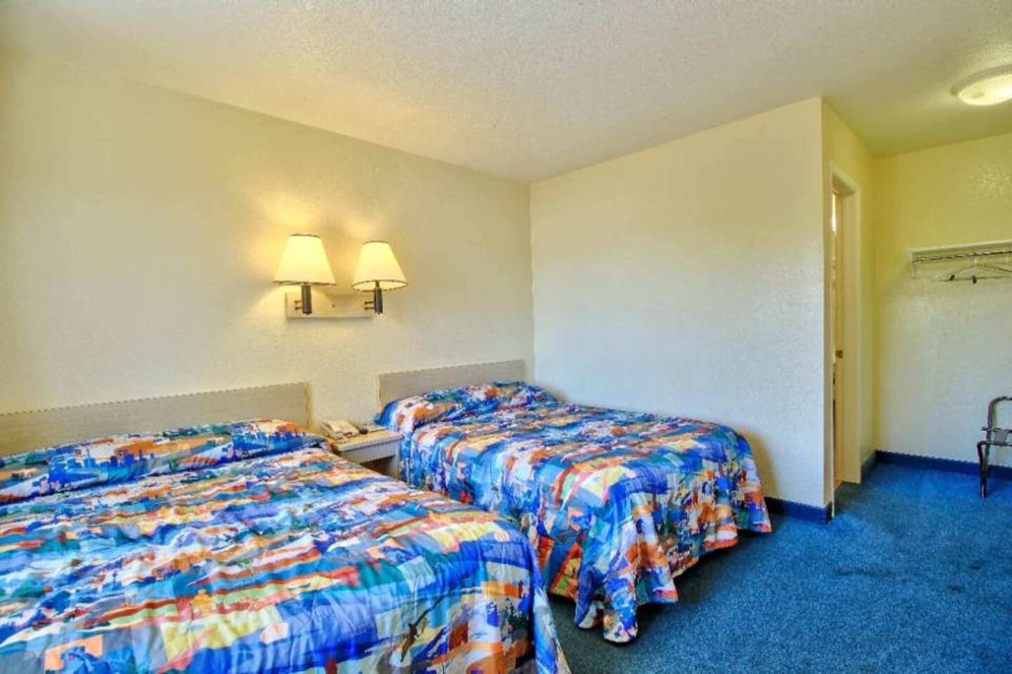 A hotel room with two beds, a desk, a telephone, and a coat rack.