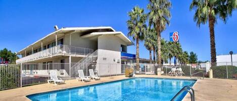 A hotel with a swimming pool, palm trees, and a clear blue sky.