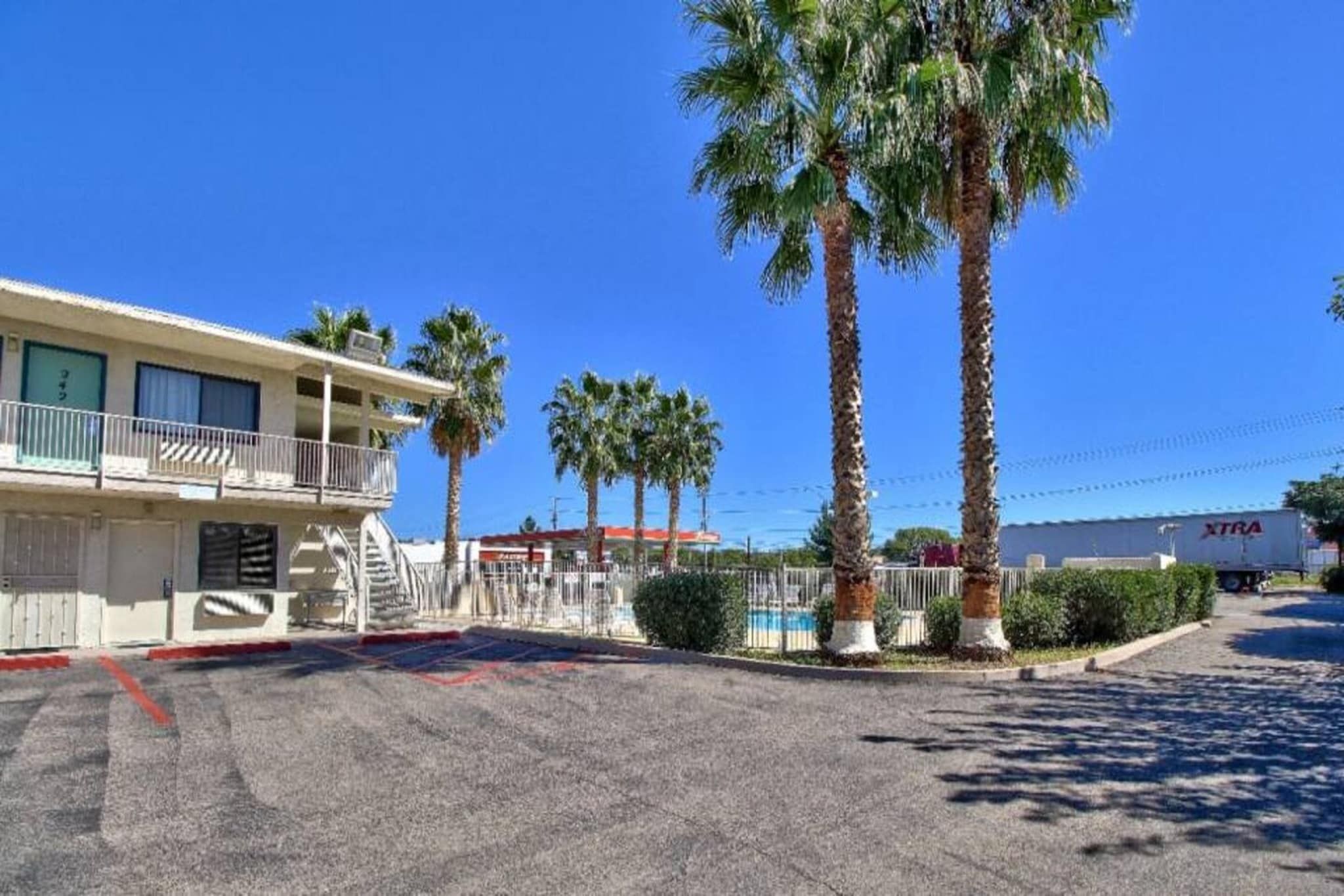 A motel with a two-story building, a fenced parking area, and palm trees.
