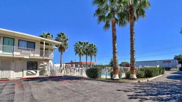 A motel with a two-story building, a fenced parking area, and palm trees.