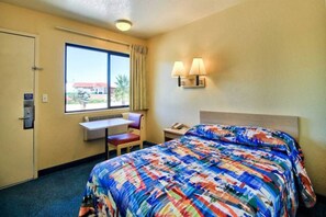 Habitació d'hotel amb un llit, una taula de treball, una cadira, una finestra i una làmpada penjada a la paret.