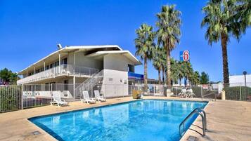 A hotel with a swimming pool, palm trees, and a clear blue sky.
