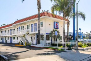 Un motel à deux étages, avec un toit recouvert de tuiles rouges, de nombreuses chambres dotées de portes bleues et un parking où l’on aperçoit, au fond, une concessionnaire Chevrolet.
