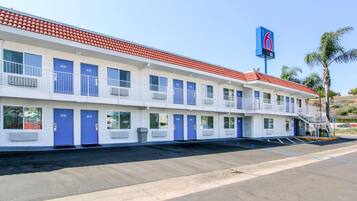 A motel with a red-tiled roof, multiple blue doors, and a sign indicating the number 6.