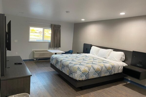 A modern hotel room with a large bed, a desk, a chair, a television, and a window with curtains.