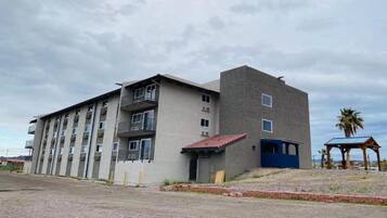 Un edificio de varios pisos con balcones y una pequeña construcción adosada con techo rojo.