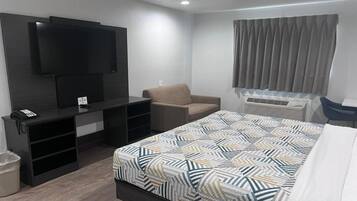 Quarto de hotel com cama, televisão na parede, cadeira, escrivaninha e janela com cortinas.