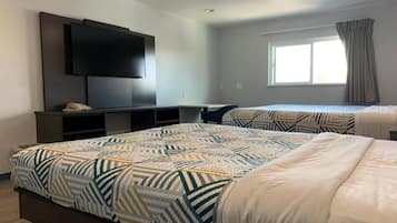 Ein Schlafzimmer mit zwei Betten, einem an der Wand befestigten Fernseher und einem Fenster mit Vorhängen.