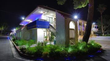 A building with a 'WELCOME' sign, a covered entrance, and a landscaped area with shrubs.