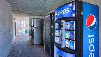 A vending machine with a Pepsi logo, a refrigerator, and a trash can in a corridor.