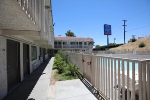 Een motel met een rij kamers, een omheind zwembadgedeelte en een heldere blauwe lucht.