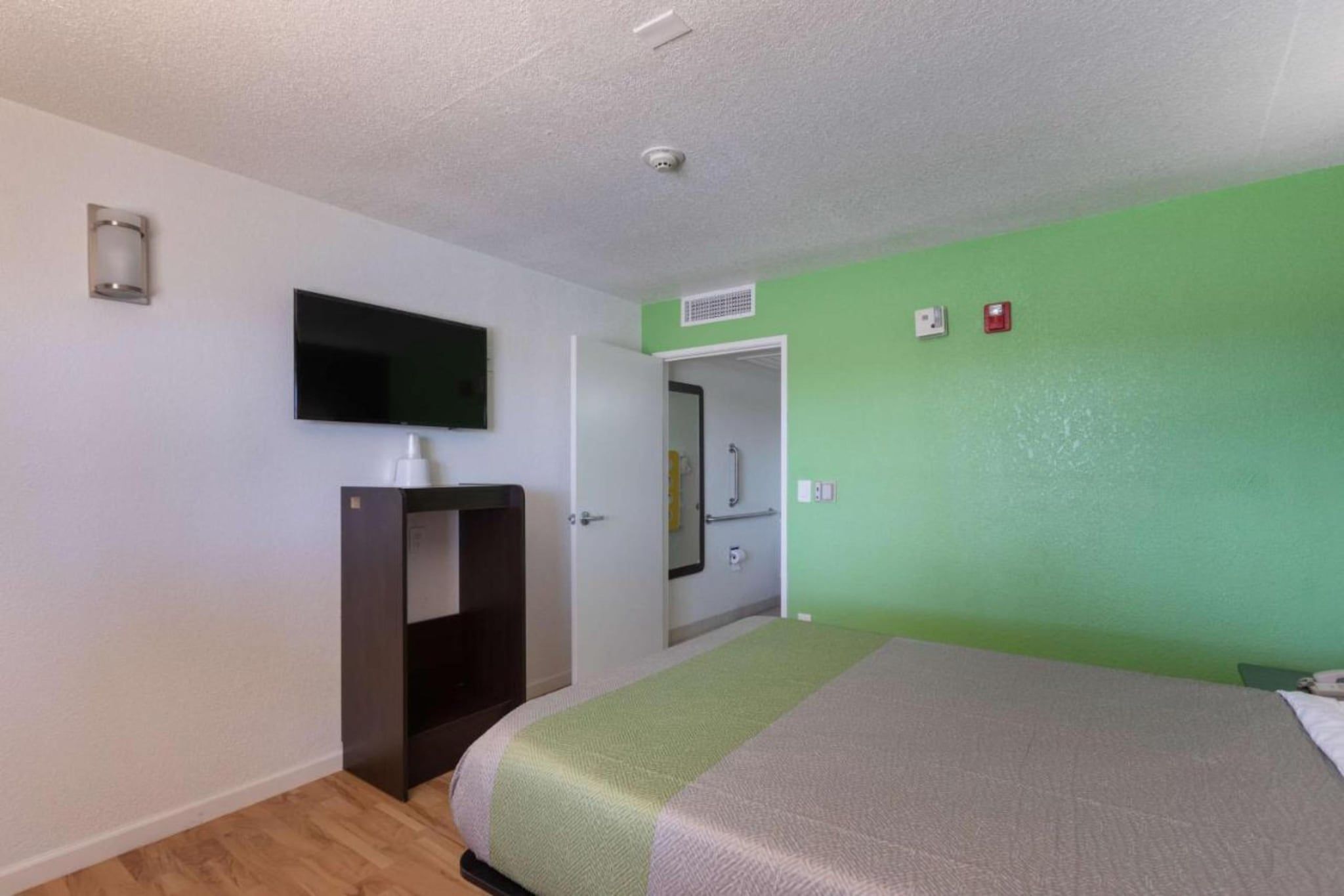 A hotel room with a bed, a television mounted on the wall, a wardrobe, and a door leading to a bathroom.