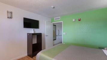 A hotel room with a bed, a television mounted on the wall, a wardrobe, and a door leading to a bathroom.