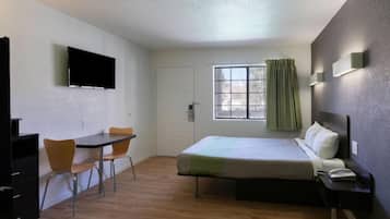 A small, clean room with a bed, a desk, a chair, a television, and a window with curtains.