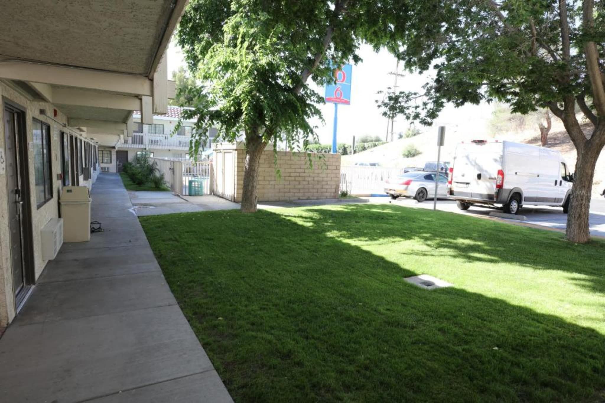 A building with a covered walkway, a grassy area, and parked vehicles.