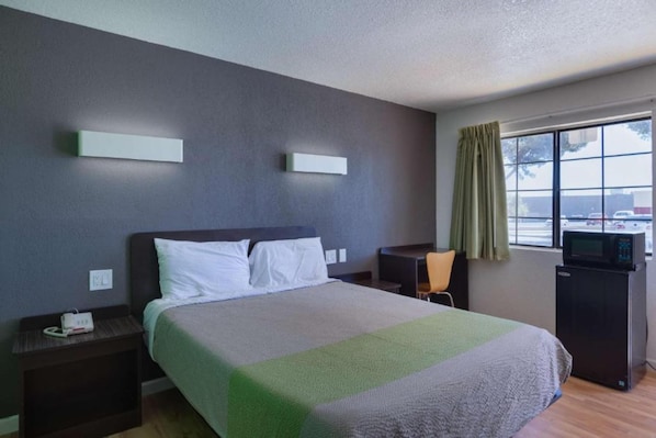 A hotel room with a bed, bedside tables, a desk, a chair, a television, and a window with curtains.